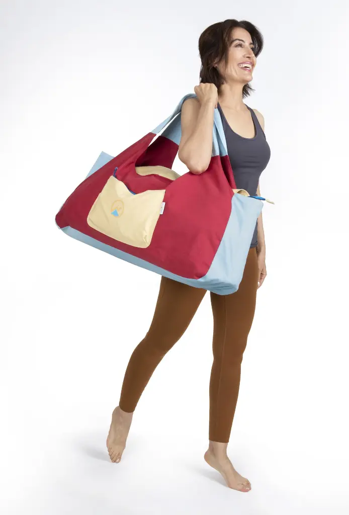 Woman holding an extra Large burgundy gym bag on her side that covers her upper half body.webp